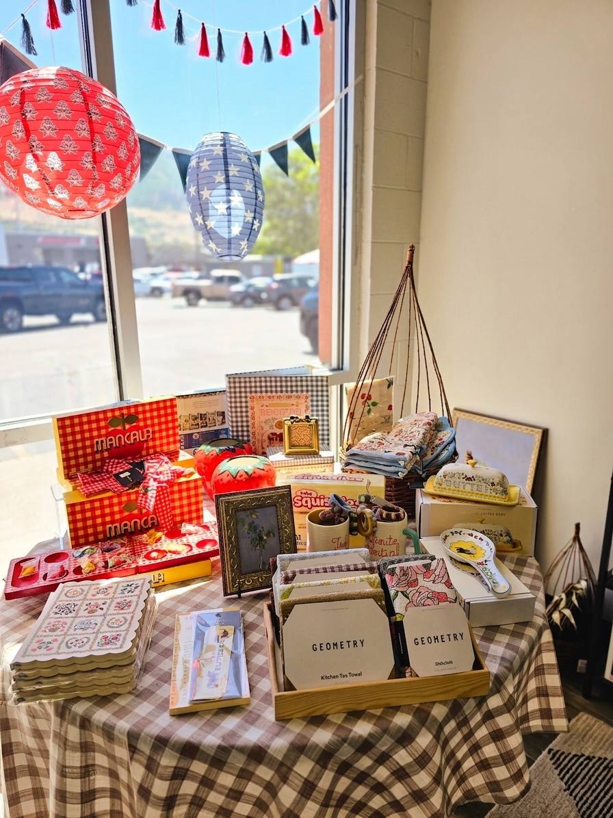 The gift shop's front-window display: red gingham games, paper lanterns, Geometry tea towels, and homeware in warm daylight